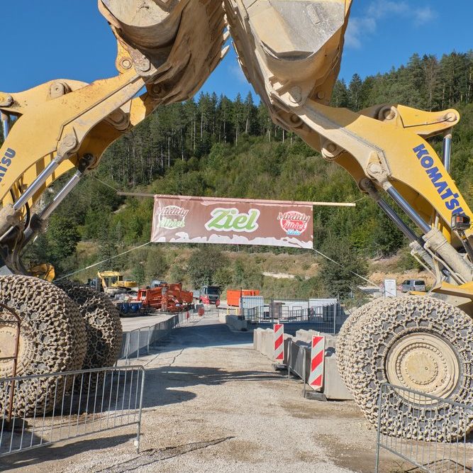 Gelände: Muddy Älbler. Großbaustelle mit zwei Baggern, die ein Banner halten, umgeben von Baustellenmaterial.